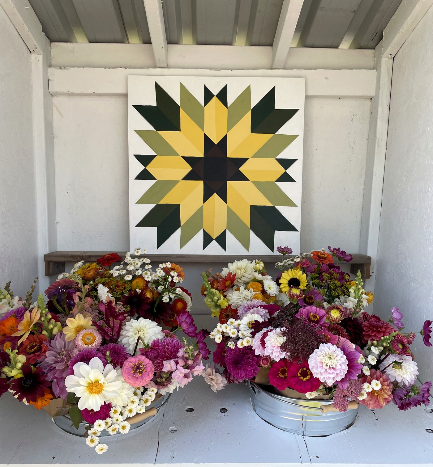 Two galvanized tubs of freshly cut bouquets on the shelf at the flower stand, under the painted barn quilt